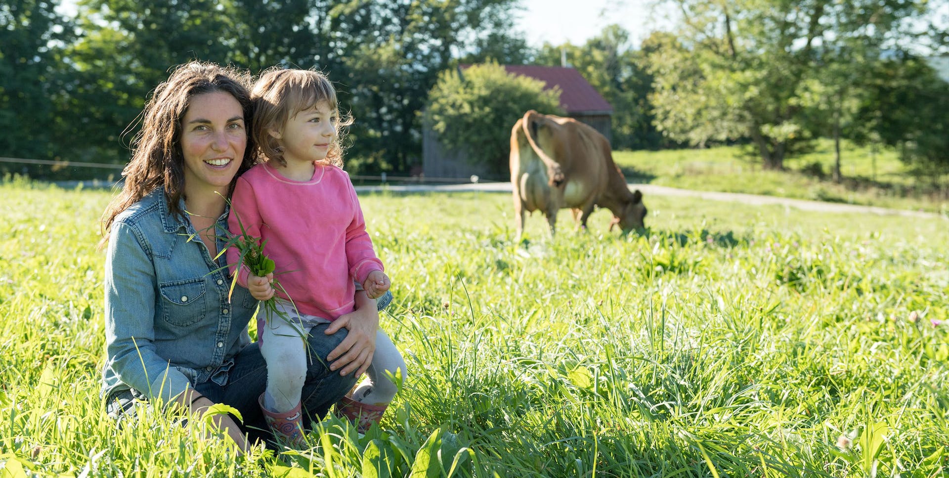 A farmer and her daughter standing in a field with a cow.