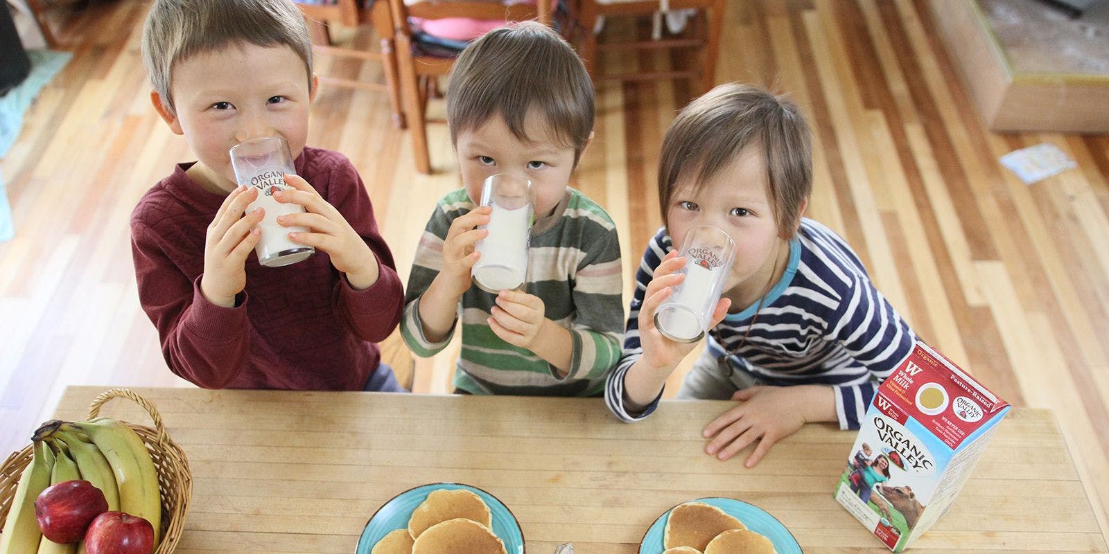 Three boys happily drink Organic Valley milk with their pancakes.