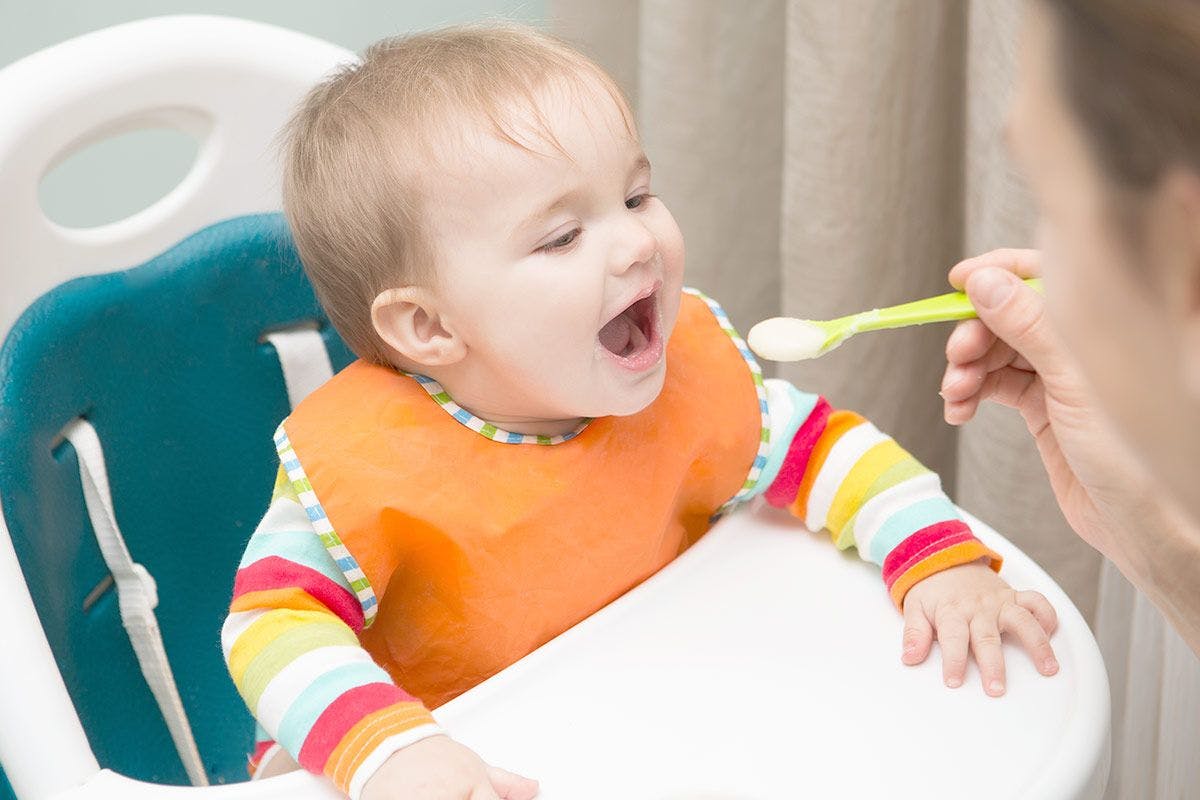 Baby eating yogurt from a spoon in a high chair.