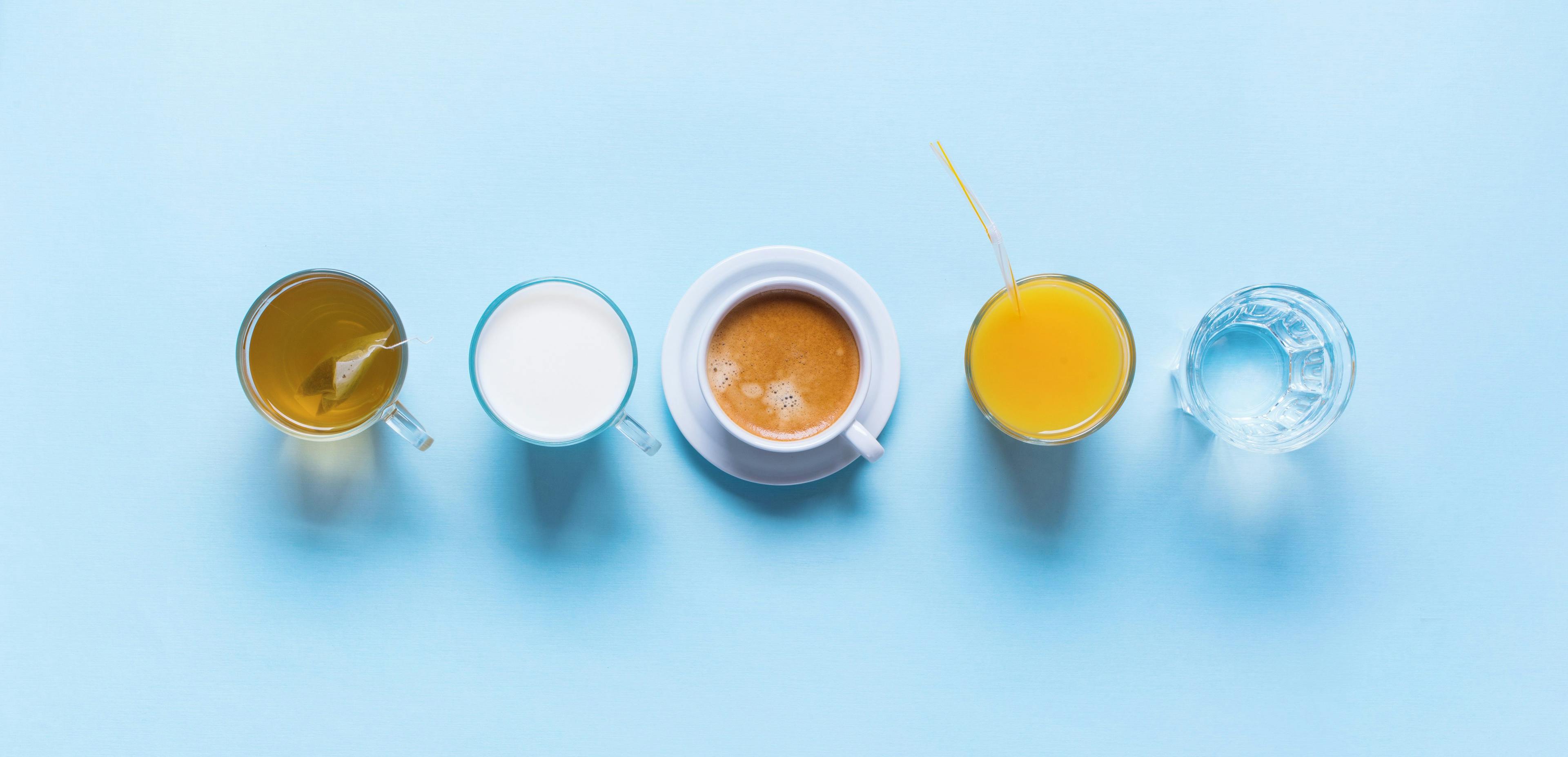 A cup of tea, milk, coffee, OJ with a straw, and water lined up.