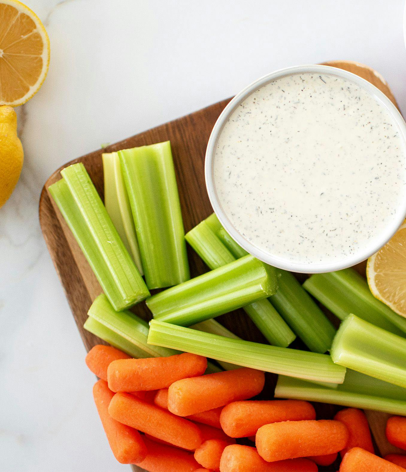 Garlic Lemon Dill Dip displayed on a cutting board with lemon, carrots and celery.
