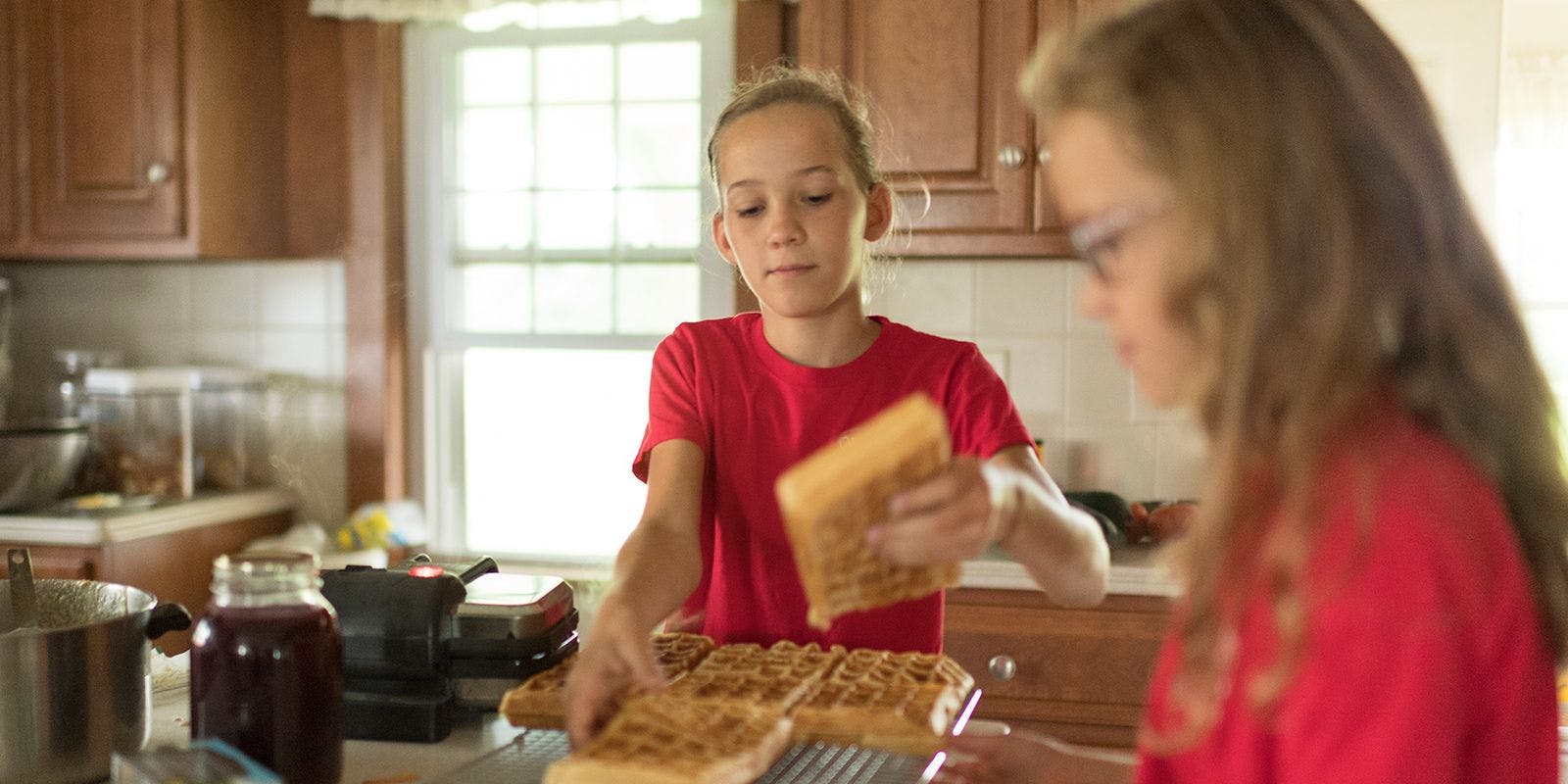 Two young girls prepare waffles in the kitchen.