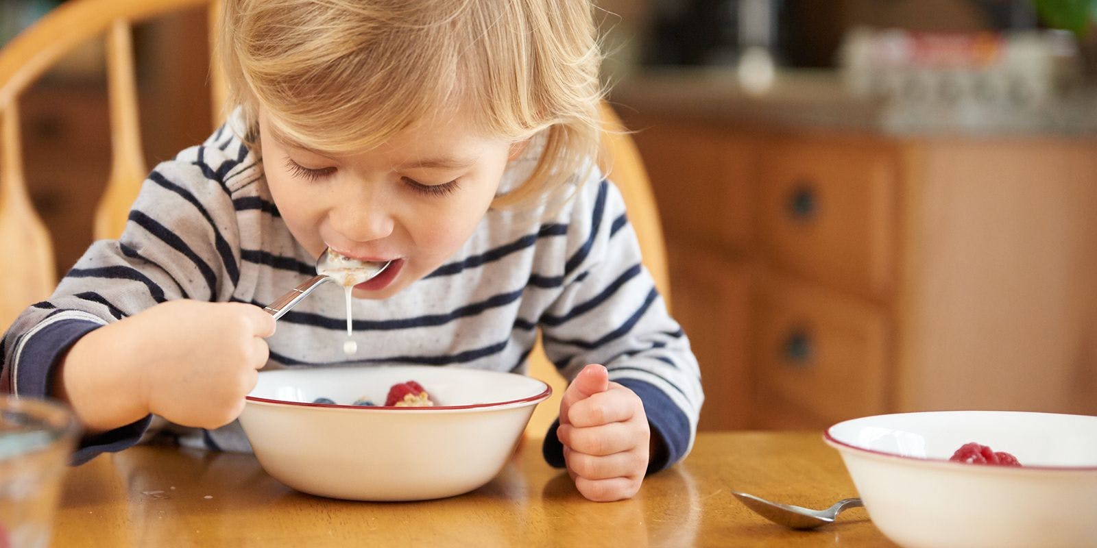 Young boy takes a spoonful of milk and cereal for breakfast.
