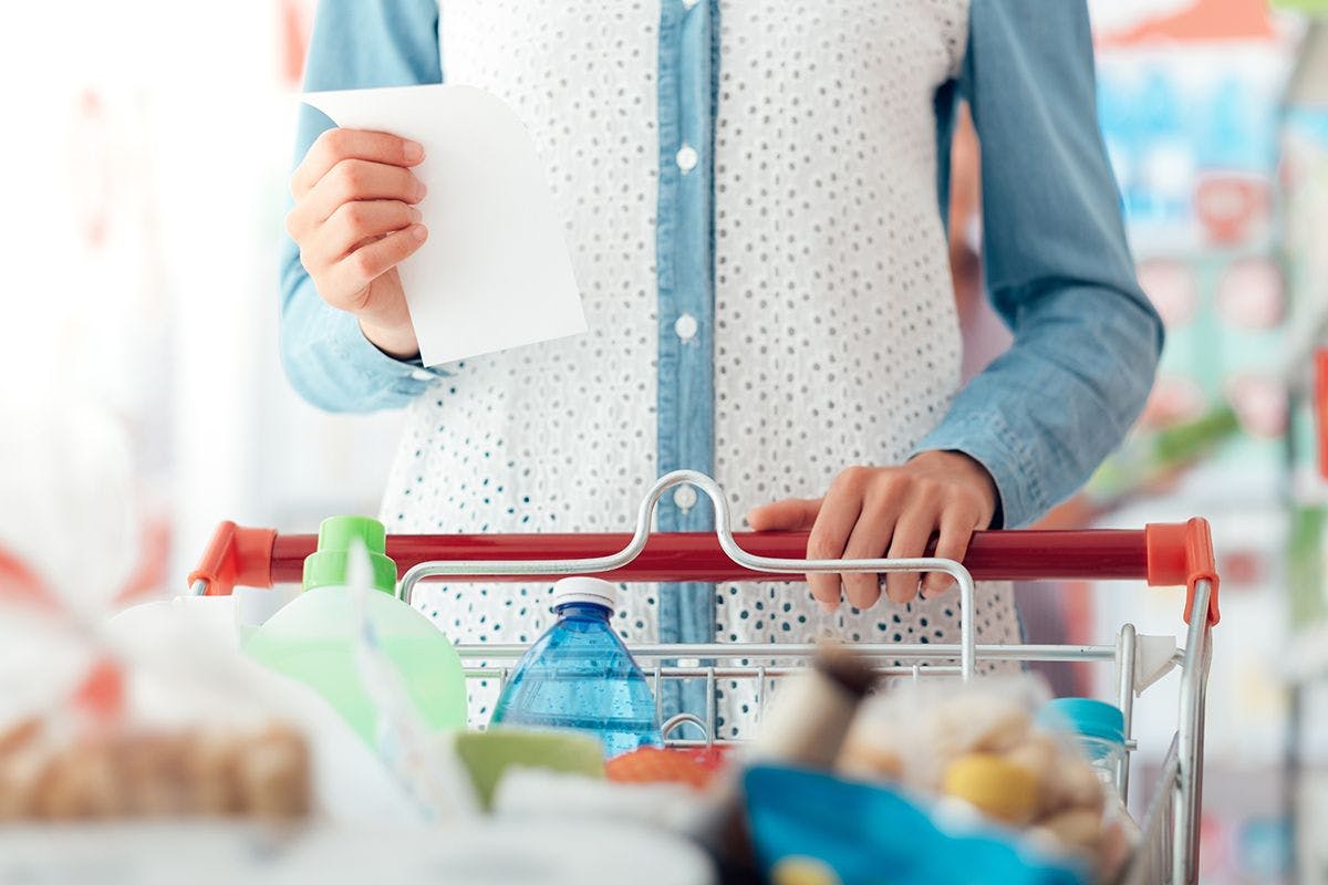 Women holds grocery list as she holds a grocery cart.