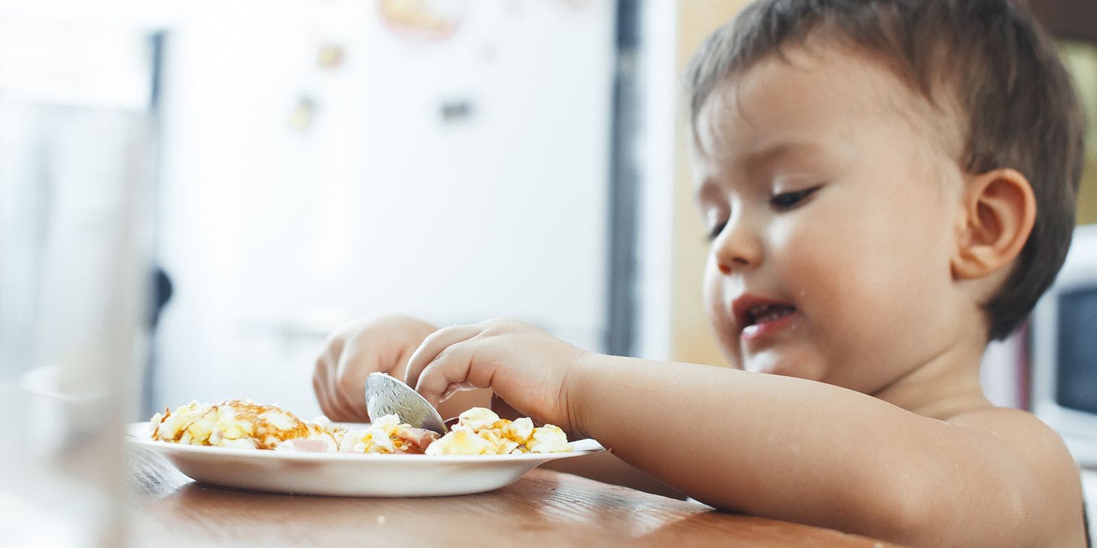 Young child eats a plate of scrambled eggs.