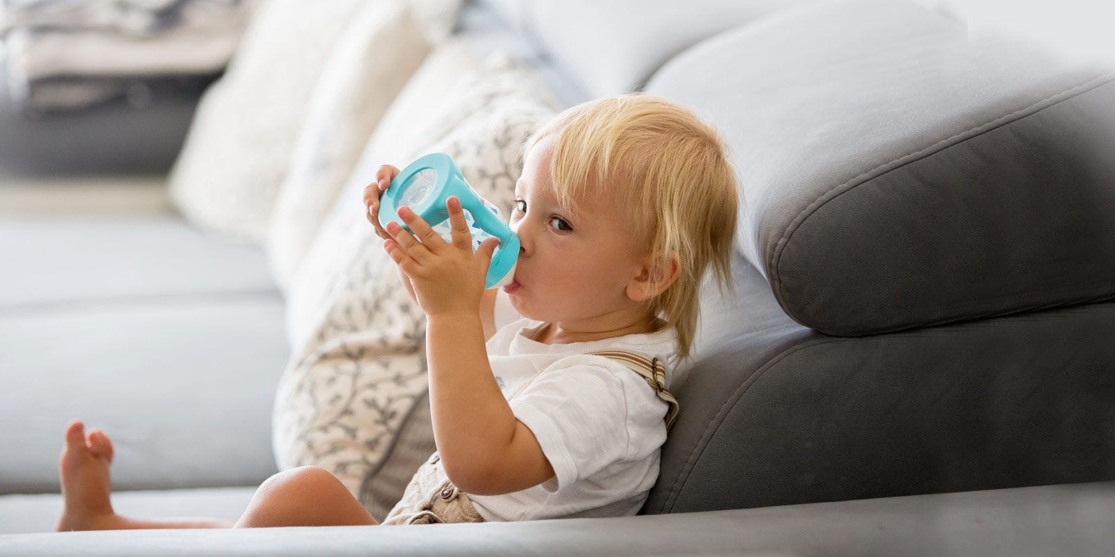 Child drinking milk in a sippy cup on the couch.