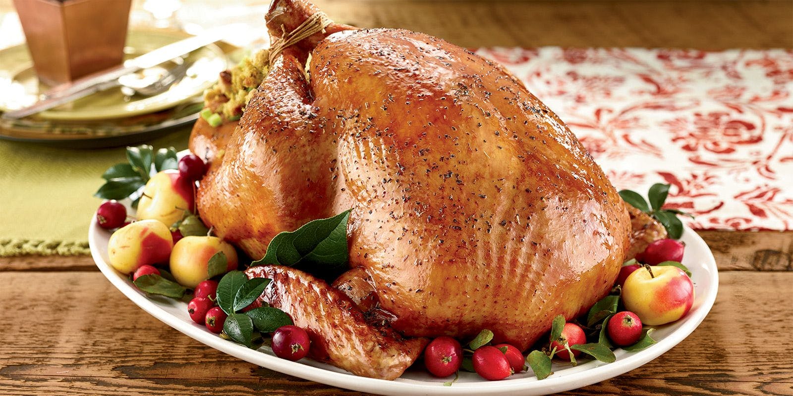 A golden brown roasted turkey on a platter surrounded by apples, cranberries and greenery.