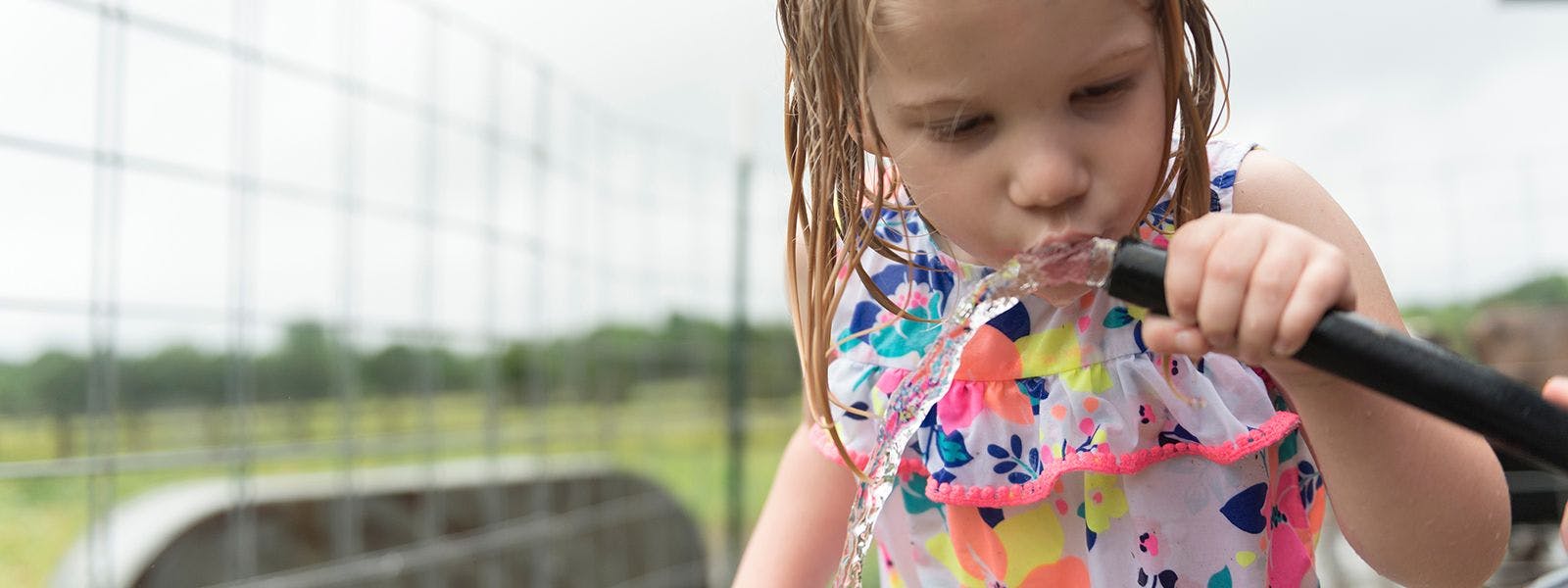 Young girl drinking water from a garden hose