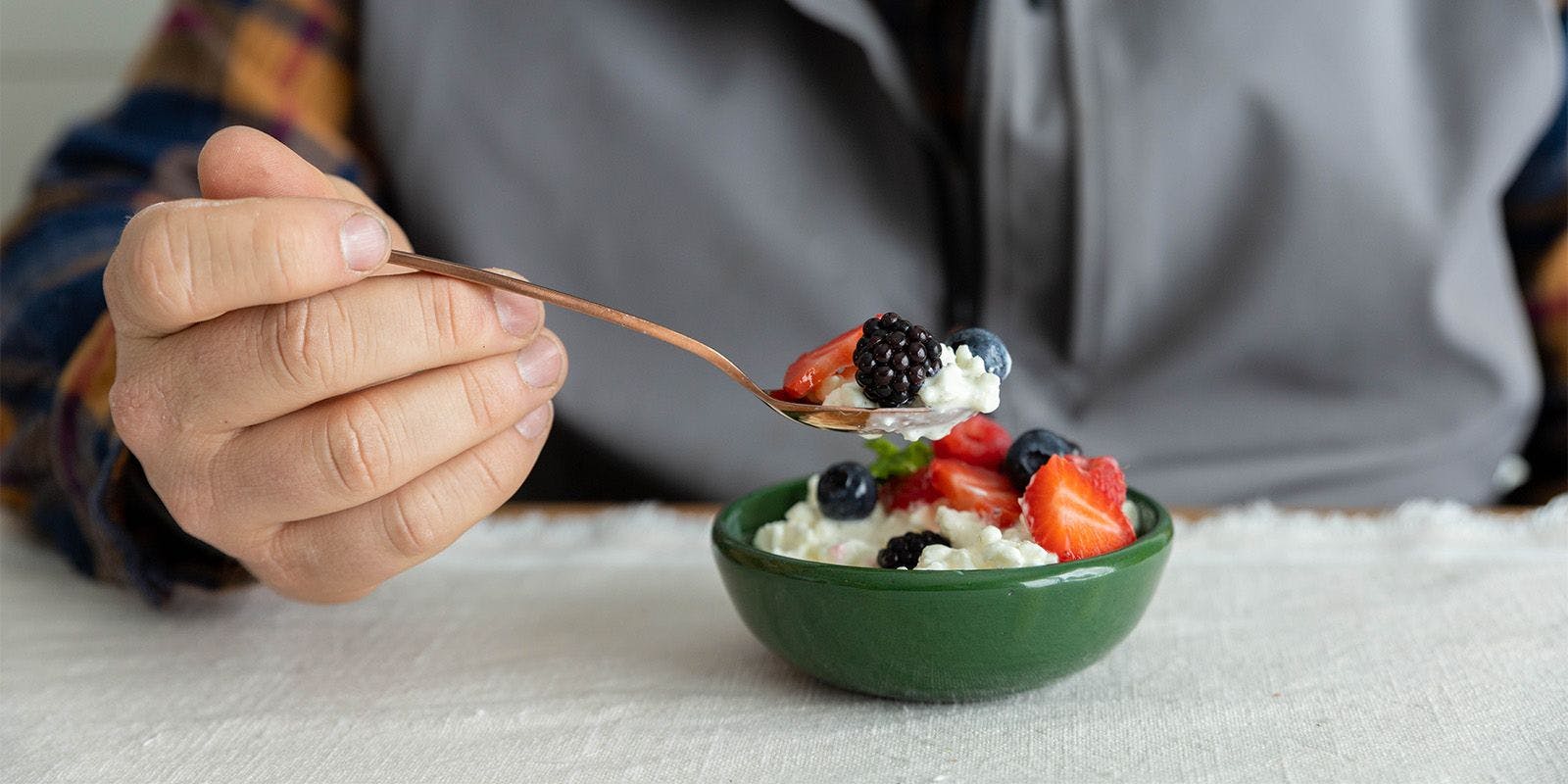 A man eats a bowl of organic cottage cheese with strawberries, blackberries and blueberries.