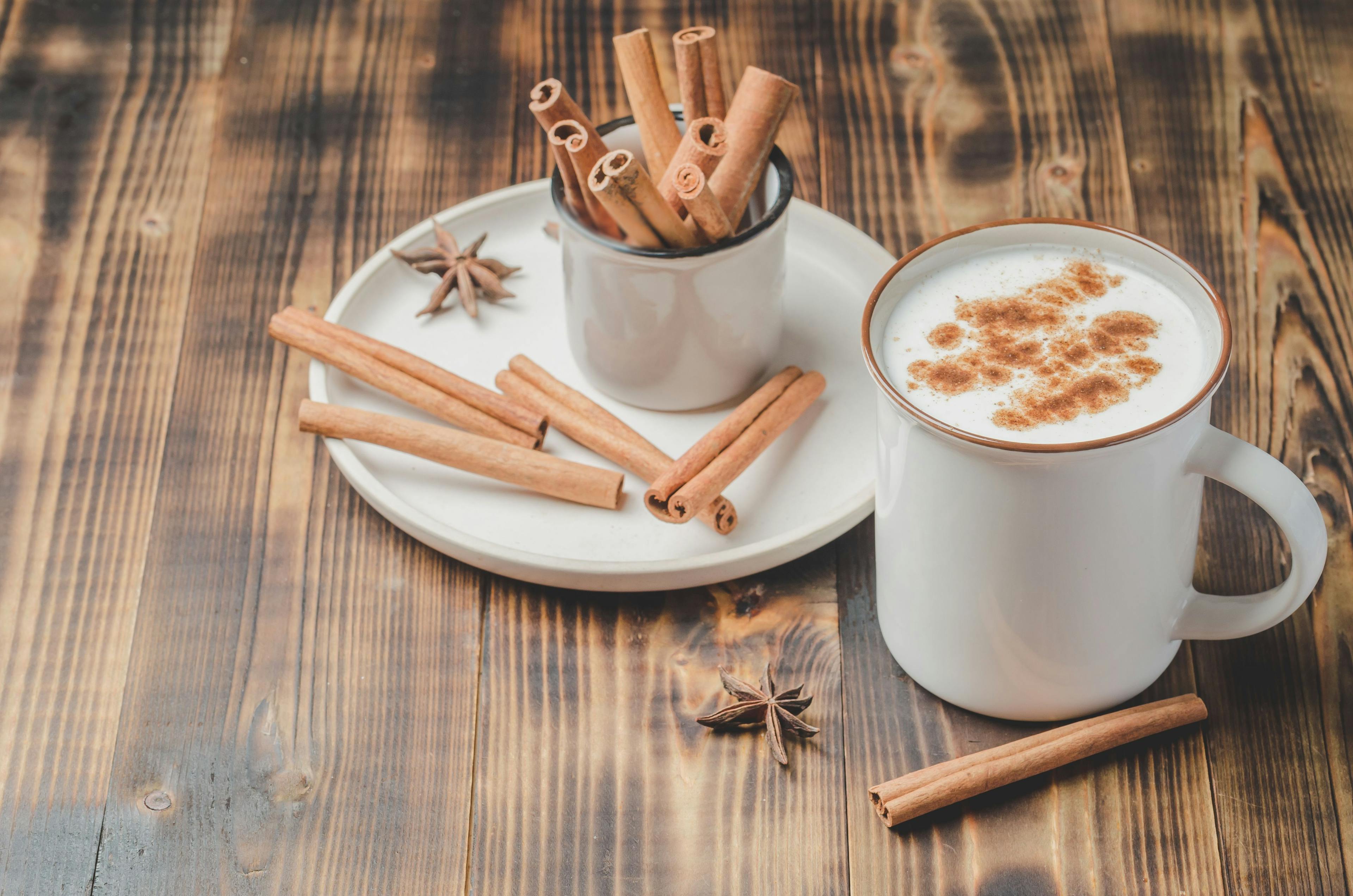 A mug of eggnog surrounded by cinnamon sticks.