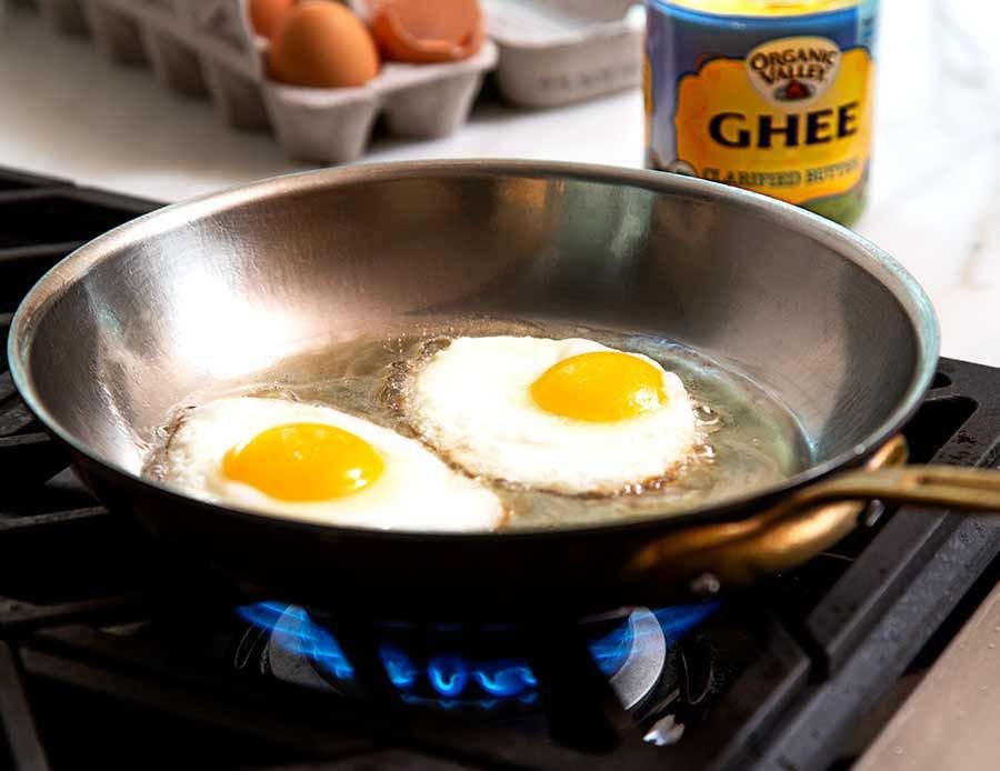 Eggs frying in a pan of ghee on the stovetop.