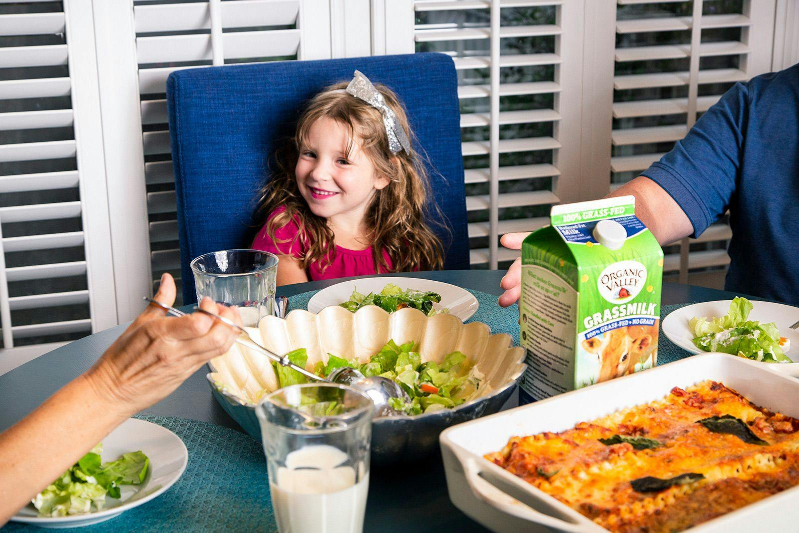 A little girl sits at the dinner table and enjoys a meal of lasagna, salad, and Organic Valley Grassmilk.