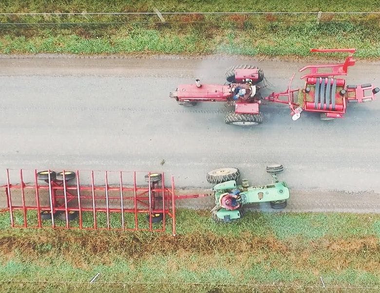 An overheard view of two tractors pulling machinery down a road. 