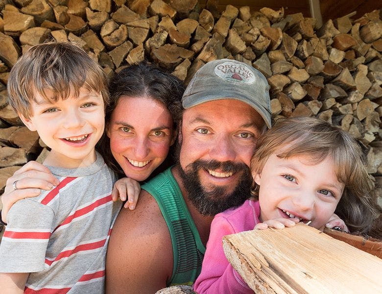 A farm family gathered in front of a pile of wood.